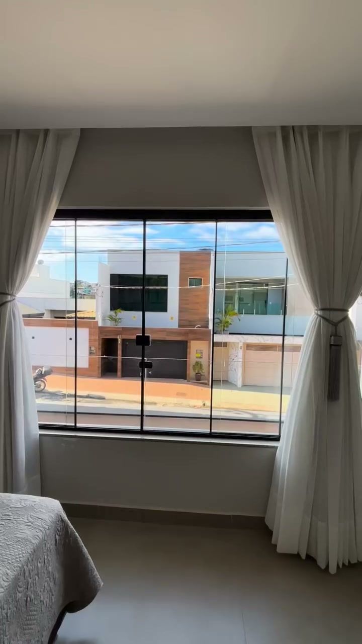 Janela ampla com cortinas cinza amarradas nas laterais